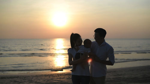 Men standing at beach during sunset