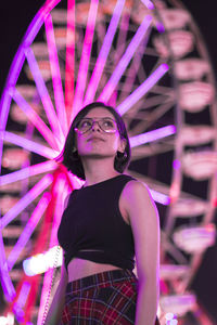 Woman standing by illuminated ferris wheel at night