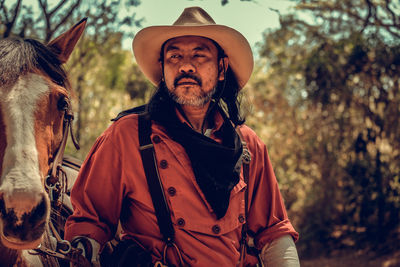 Serious man with horse standing in forest