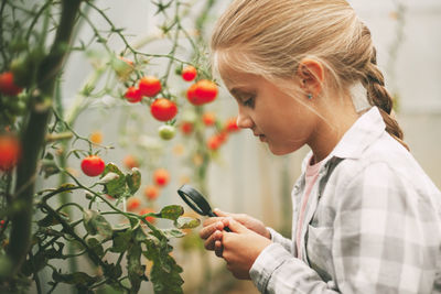 A beautiful little girl examines small cherry tomatoes through a magnifying glass. curious children.