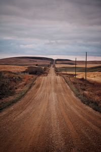 Rural dirt road passing through landscape against sky