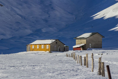 Houses on snowy field against blue sky on sunny day