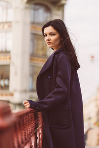 Portrait of young woman standing by railing