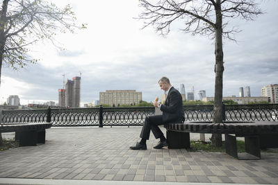 Businessman having lunch sitting on seat at promenade