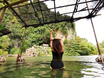 Rear view of woman standing by lake in forest