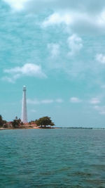 Lighthouse in sea against cloudy sky