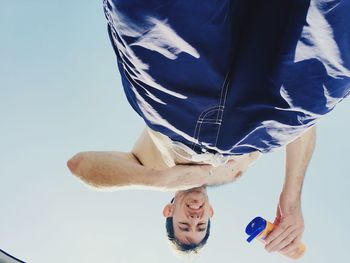 Low angle view of man applying lotion against clear sky