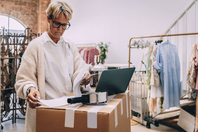 Focused female owner looking at inventory list while working in clothing store