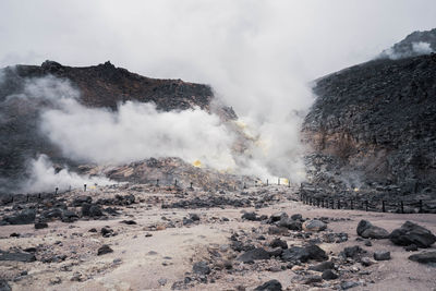 Smoke emitting volcanic landscape against sky