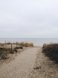 Footpath leading towards sea against sky