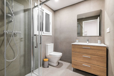 Modern refurbished bathroom with shower zone, toilet, wooden base with white sink and mirror.