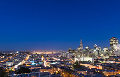 High angle view of city lit up against blue sky