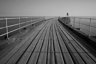 Wooden footbridge over sea against clear sky