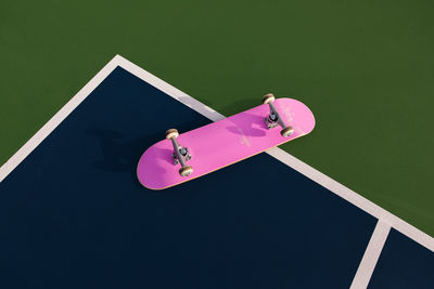 Pink skateboard in direct sunlight on tennis court