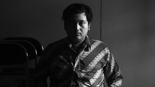 Portrait of serious young man standing against wall at home