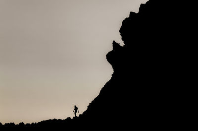 Silhouette people on rock against sky during sunset