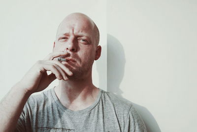 Portrait of mid adult man smoking cigarette against wall