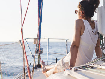 Rear view of mid adult woman looking at sea view while sitting in sailboat against clear sky