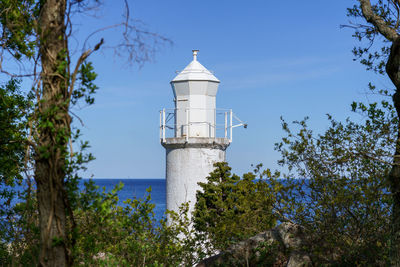 Lighthouse amidst trees and buildings against sky
