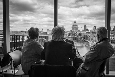 Rear view of people looking at cityscape through window