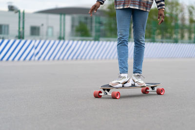 Woman on longboard. cropped image of black female wear trendy sneakers shoes and jeans on skateboard