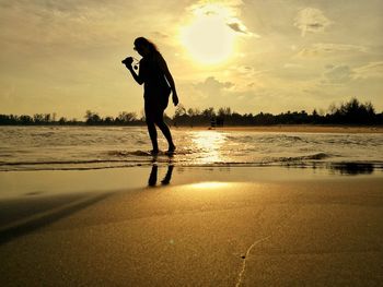 Silhouette man standing on beach against sky during sunset