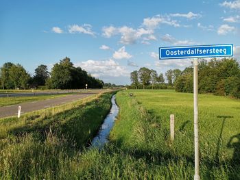 Road sign on field against sky