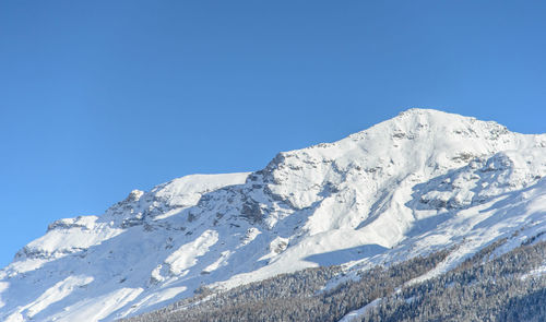 Low angle view of snowcapped mountain against clear blue sky