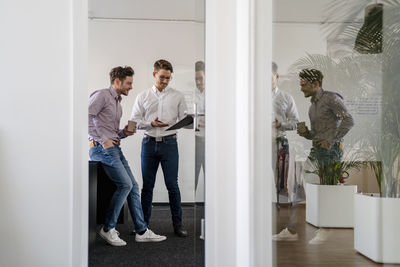 Male entrepreneurs discussing over clipboard seen through doorway at office