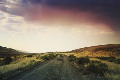 Empty road on field against sky during sunset