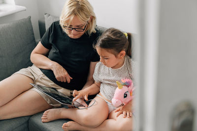 Woman with digital tablet sitting with granddaughter at home