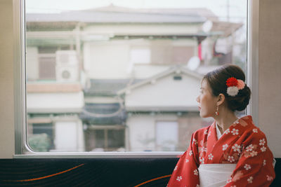 Woman in kimono looking through window at home
