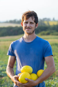 Portrait of farmer holding fruits while standing on land