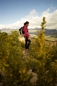 Side view of hiker standing on mountain by plants against sky