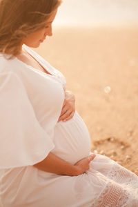 Midsection of pregnant woman sitting at beach