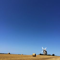 Windmills on landscape against clear blue sky