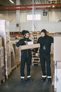 Female entrepreneur holding packages while discussing with male colleague in logistics warehouse