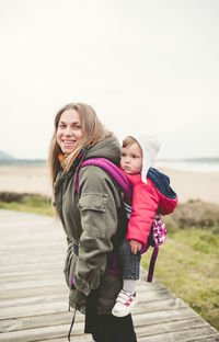 Side view portrait of smiling mother carrying baby boy on boardwalk