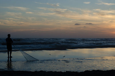 Silhouette man standing on beach against sky during sunset