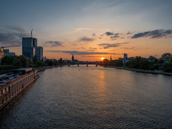 River amidst buildings against sky during sunset