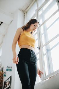 Low angle view of young woman standing by window at home