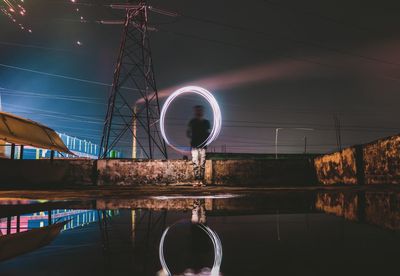 Man with wire wool by water against sky at night