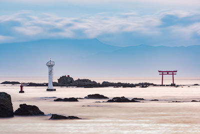 Lighthouse on beach by sea against sky