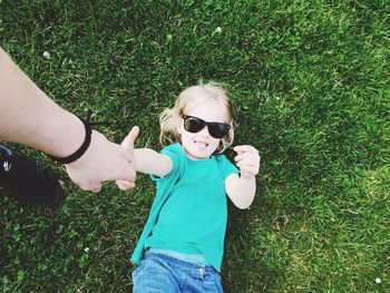 Cropped hand of woman touching daughter lying on grassy field