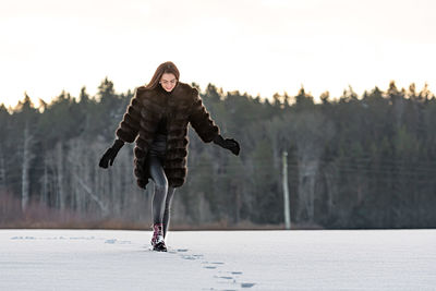 A cheerful woman in a warm fur coat walks across the open field leaving footprint in the snow