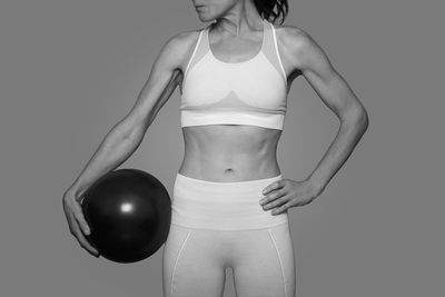 Fit woman standing holding a pilates ball, black and white.