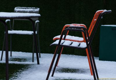 Snow on empty metallic chairs and table against fence in back yard