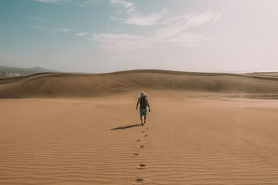 Rear view of man walking on desert against sky