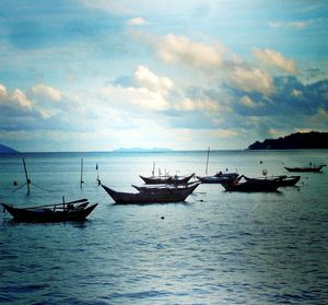 Boats in sea against cloudy sky