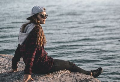 Smiling young woman sitting on rock at sea shore